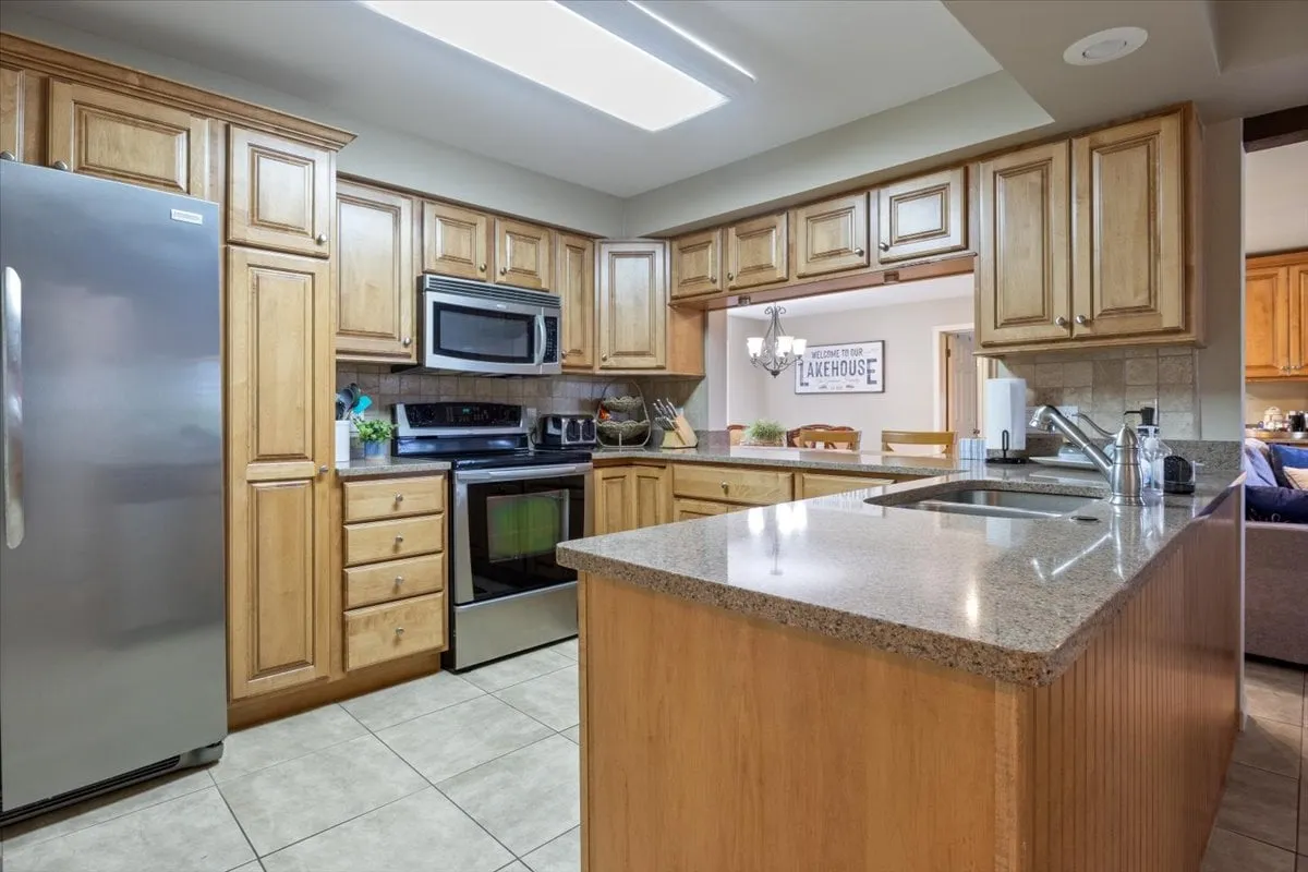 A fully equipped kitchen featuring stainless steel appliances, a granite countertop, wooden cabinetry, and a central island. The setting is perfect for preparing group meals, baking treats, or mixing drinks at the wet bar, with enough space for several people to participate in meal prep together.