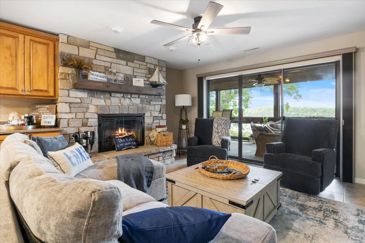 A bright, welcoming living area featuring plush sofas arranged around a modern electric fireplace. Large windows frame beautiful lake views, allowing natural light to flood the space. The setting hints at people relaxing with coffee, reading, or gathering for games, creating a sense of homey warmth.