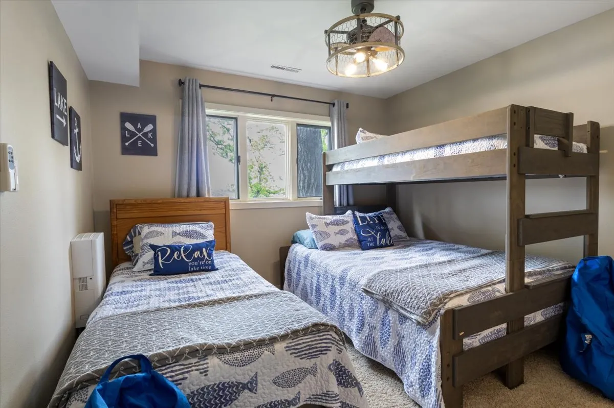 A bright, relaxed bunk room scene featuring a sturdy bunk bed adorned with decorative pillows and a window letting in natural light. The space feels calm and practical, perfect for sleepovers, reading, or quiet afternoon games.