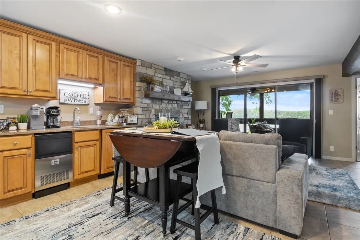 An open kitchen and seating area with a large island, stone wall, and generous windows showcasing outdoor light. There’s ample room for families to gather, prepare meals, and socialize while enjoying glimpses of the natural landscape beyond.