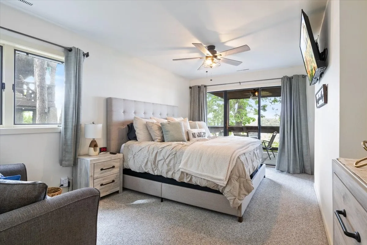 This image depicts a well-appointed bedroom featuring a comfortable bed with decorative pillows, a cozy seating area, and large windows that frame an inviting outdoor view. The atmosphere is tranquil and ideal for unwinding, hinting at a serene retreat for adults seeking relaxation and privacy.