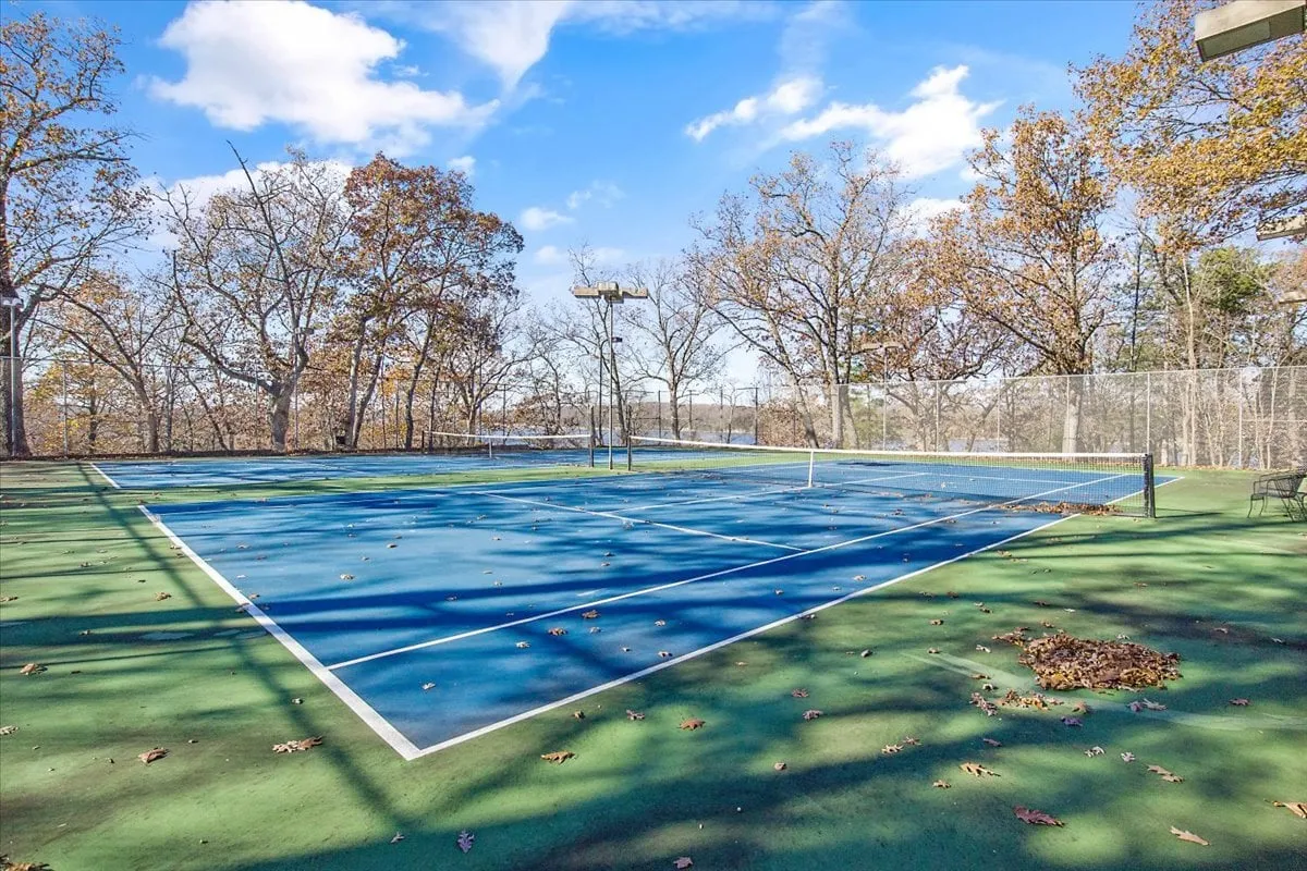 An energetic outdoor tennis court set amidst lush, mature trees. The court is well-maintained and ready for play, capturing the excitement of outdoor activity and friendly competition.